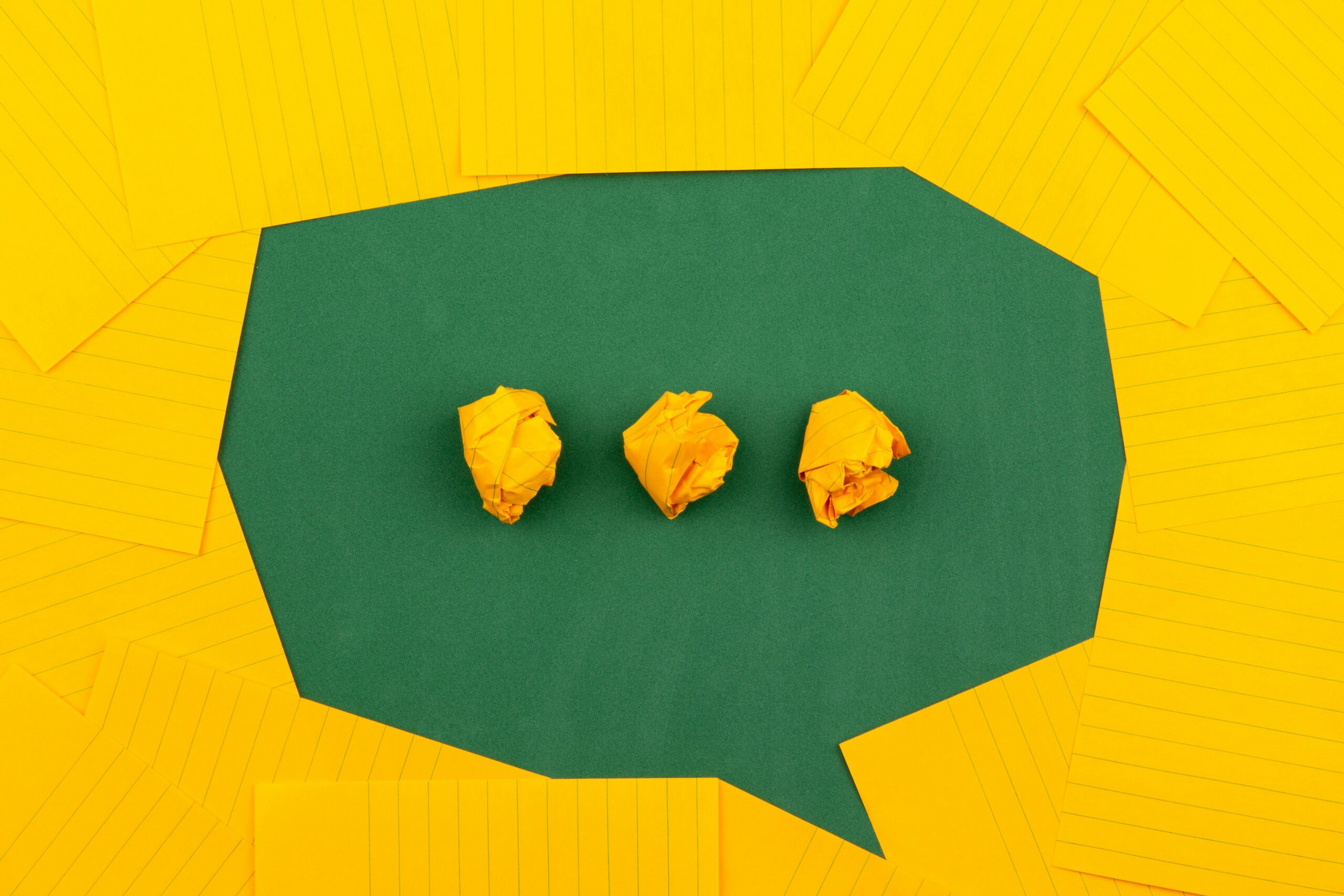 three crumpled yellow papers on green surface surrounded by yellow lined papers three crumpled yellow papers on green surface surrounded by yellow lined papers